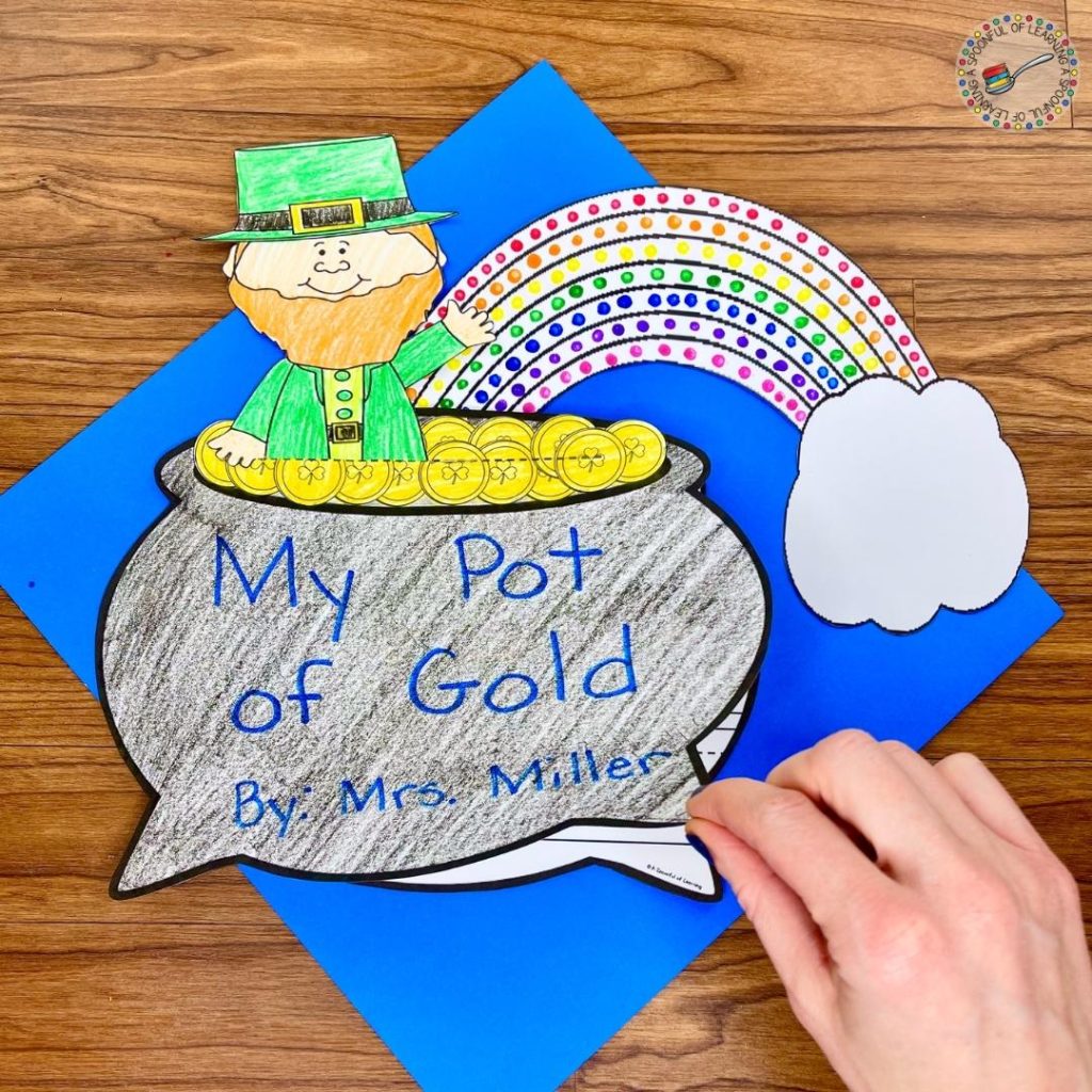 A creative writing activity where students write their own leprechaun story. This is the cover of their story that has a painted rainbow, a pot of gold with the title of their story, and a leprechaun coming out of the pot of gold.