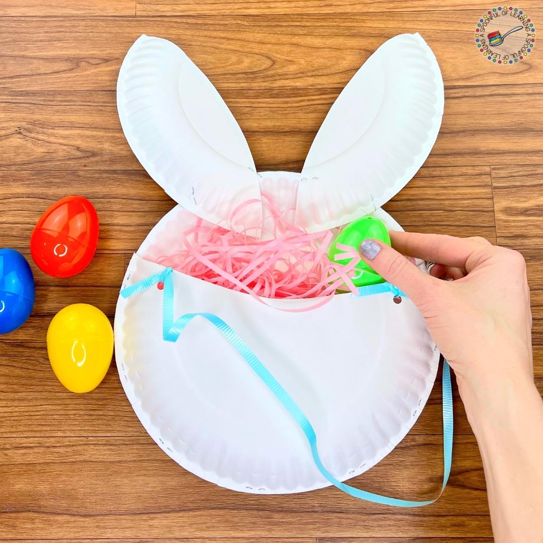 Placing plastic Easter eggs in the Easter Bunny basket craft that is made out of paper plates.