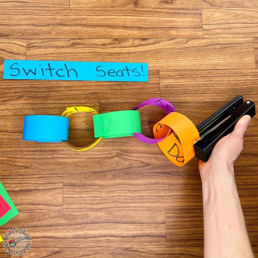 A paper strip says "switch seats" while someone staples a paper chain.